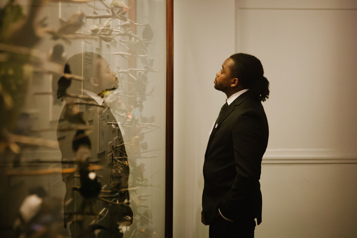 A man wearing a black suit stands looking into a exhibition display case.