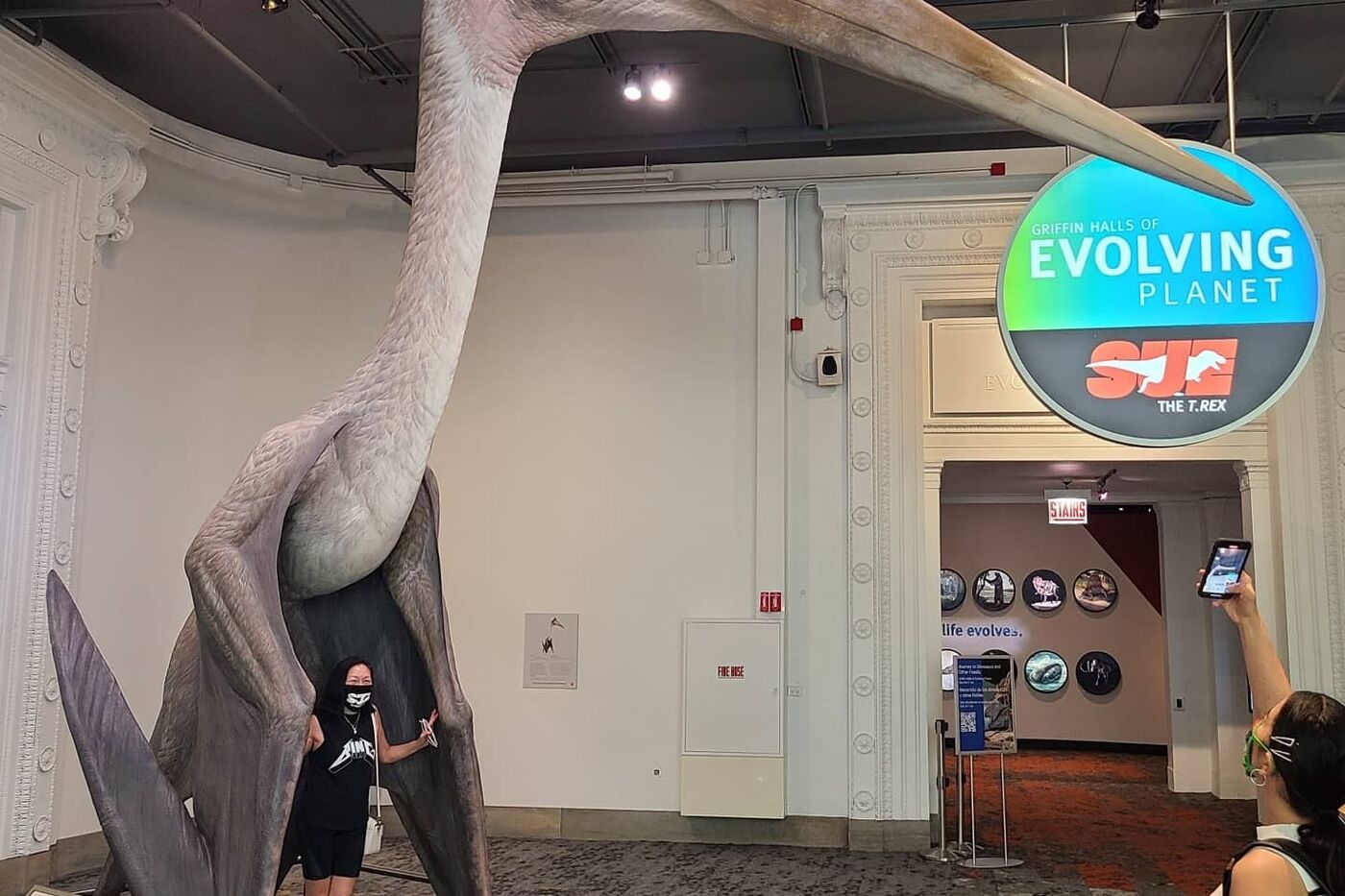 A visitor stands beneath the Queztalcoatlus model while another takes a photograph.