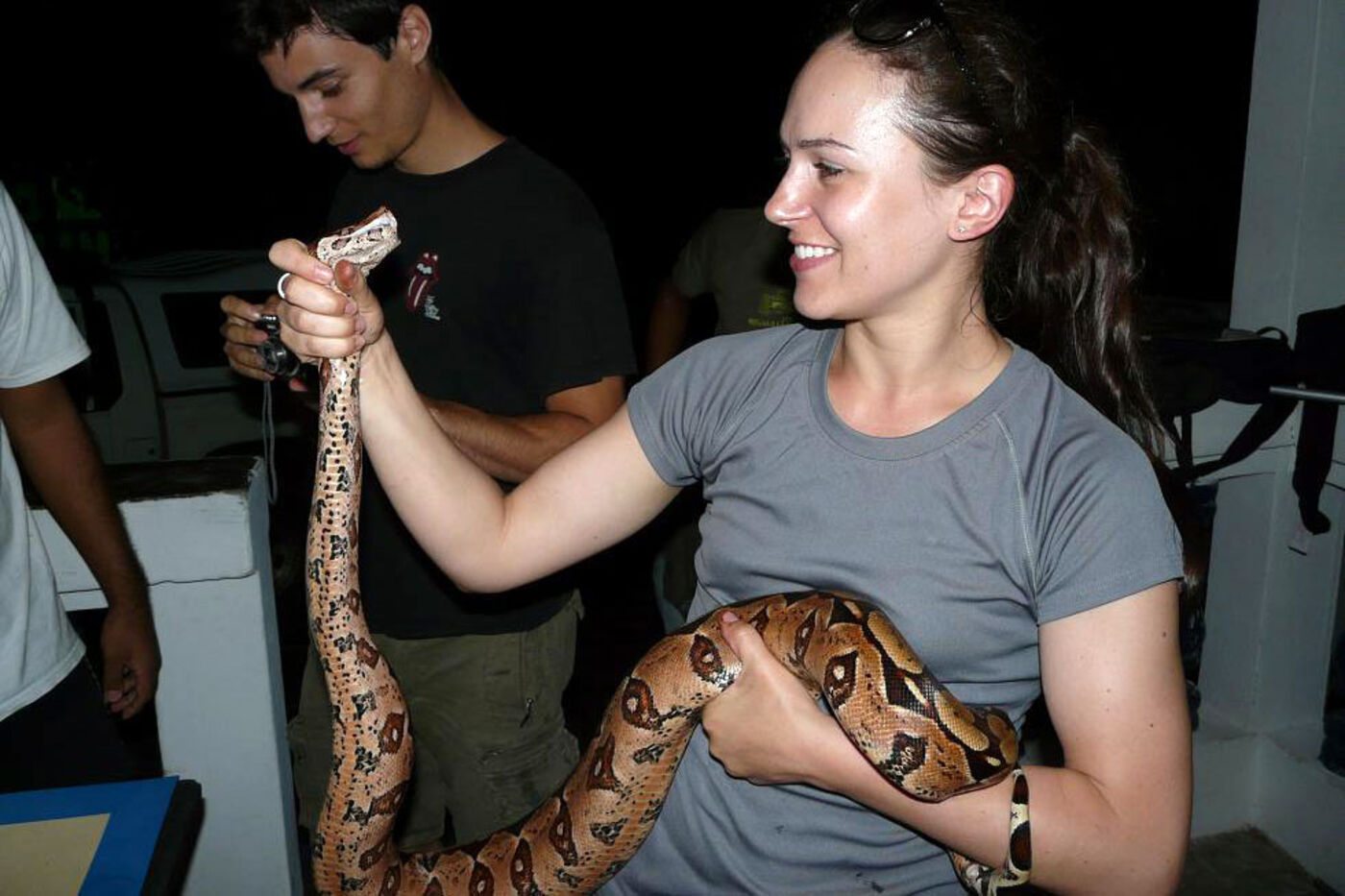 A woman holds a large boa constrictor, its head in her hands as she looks at it smiling.