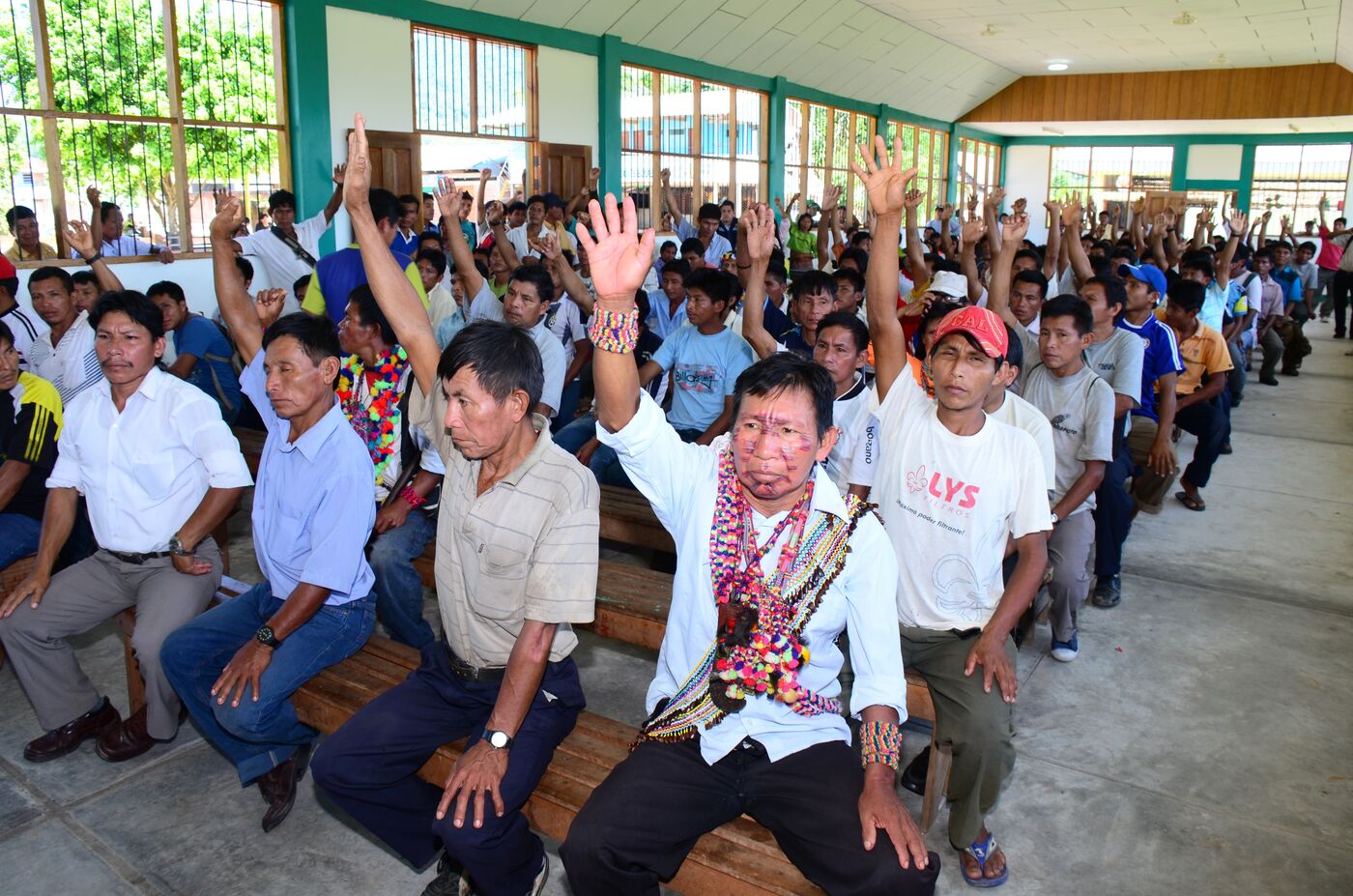 A room full of men sitting on benches with one arm raised over their heads, like in a classroom.