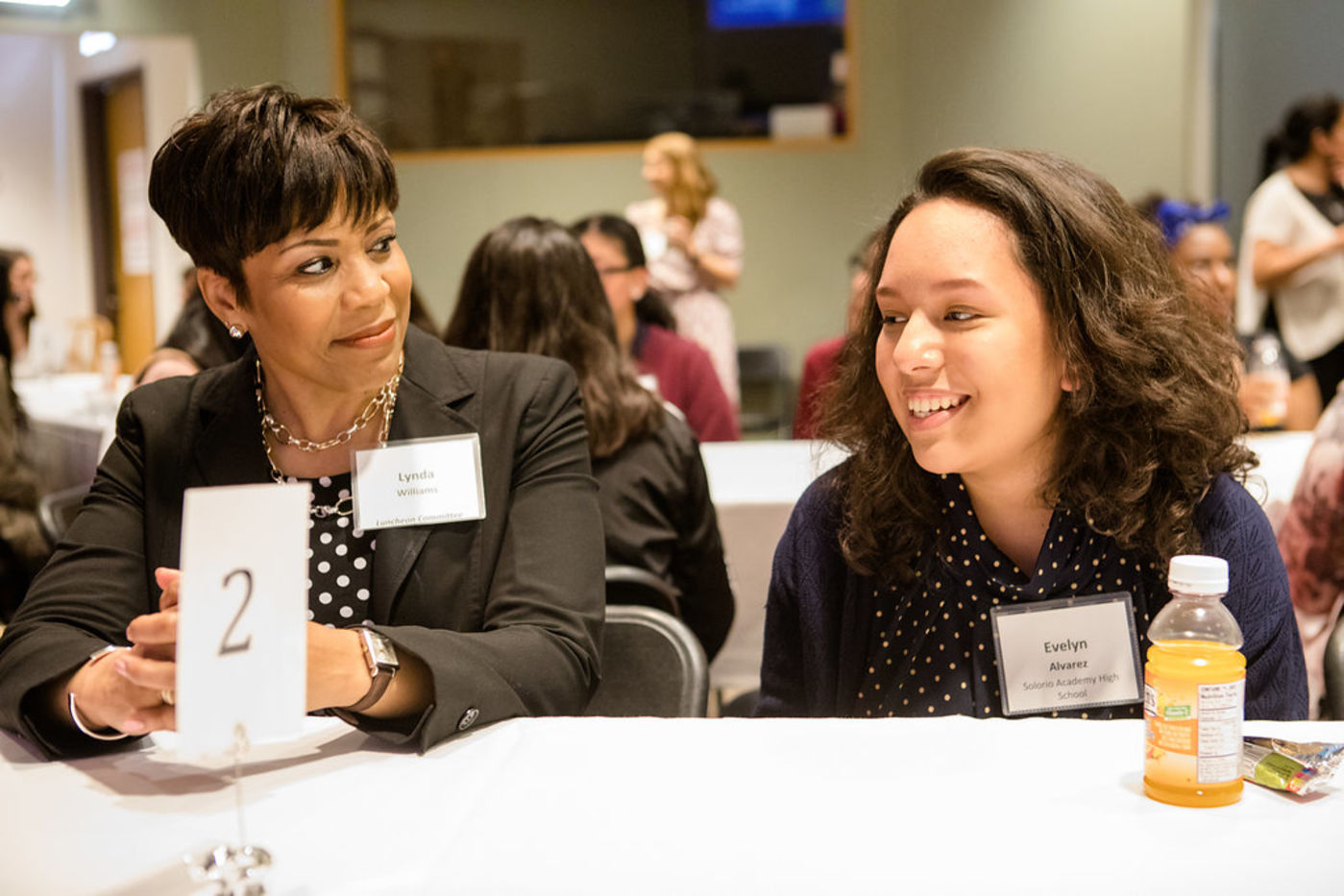 A Women’s Board member sits with a female high school student at an event.
