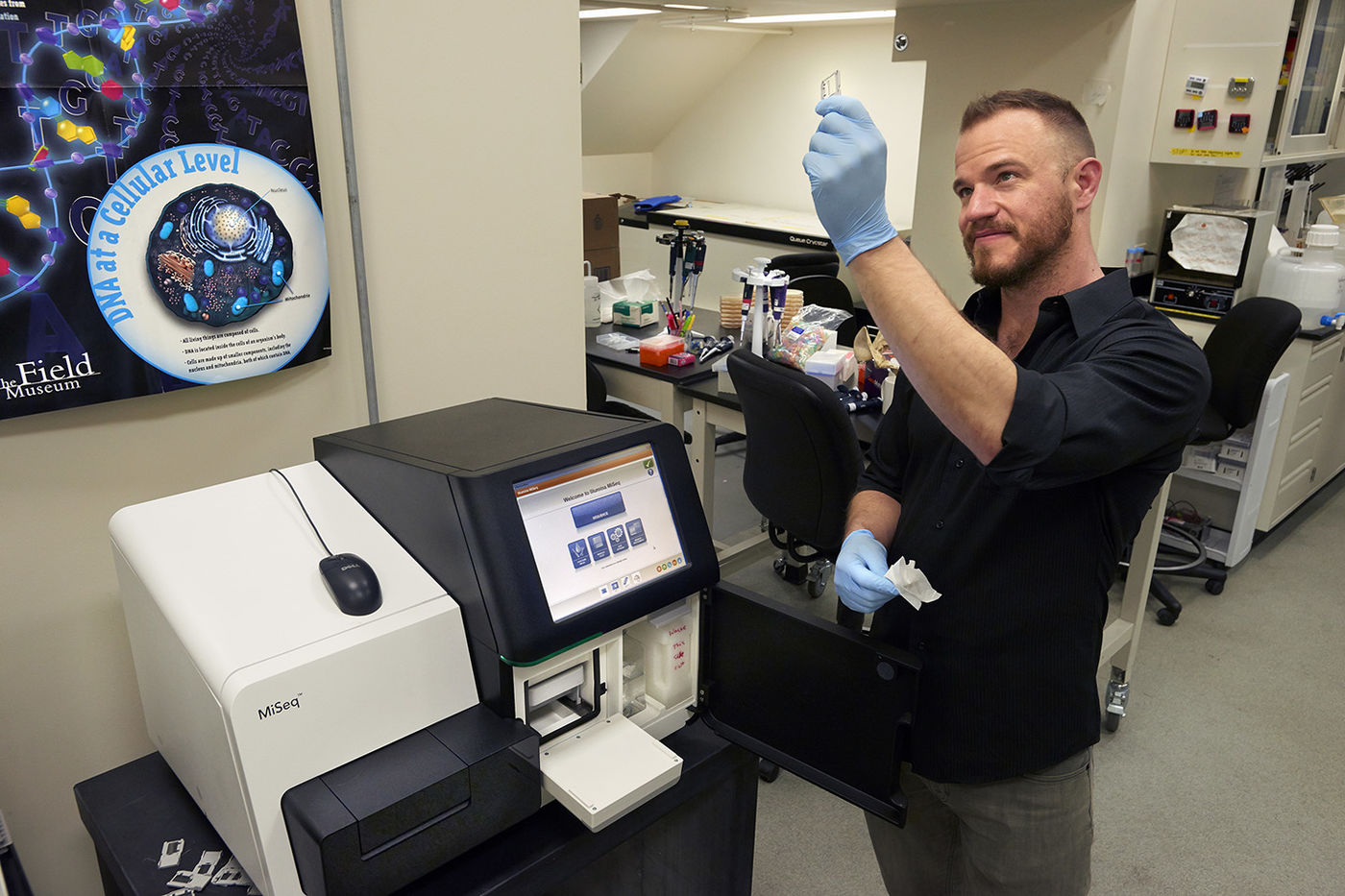 a man holding a laboratory sample up to the light in front of a MiSeq machine