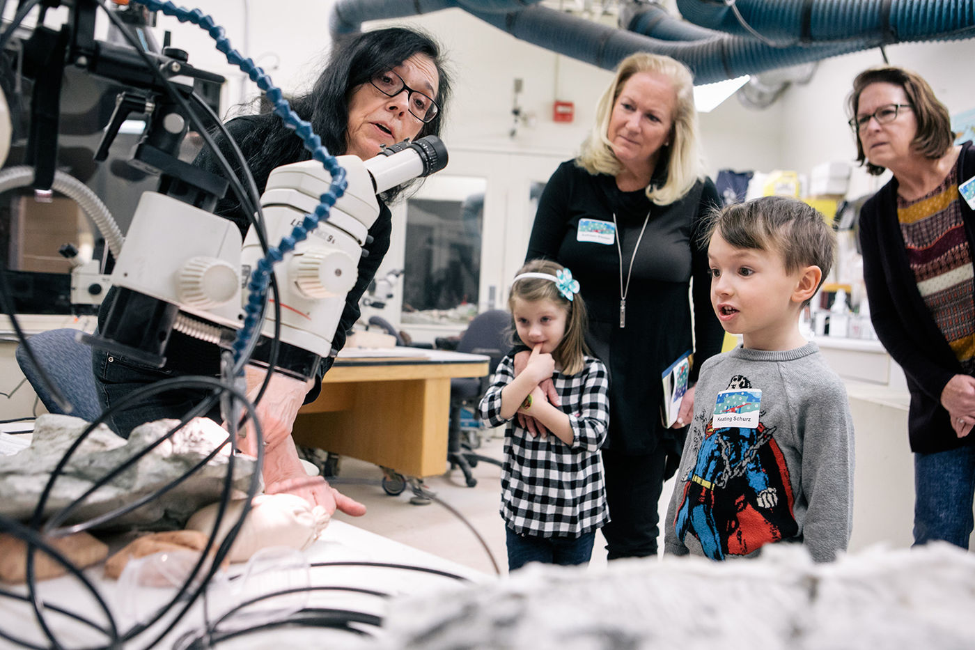 A museum staff member showing lab equipment to two women and two children.