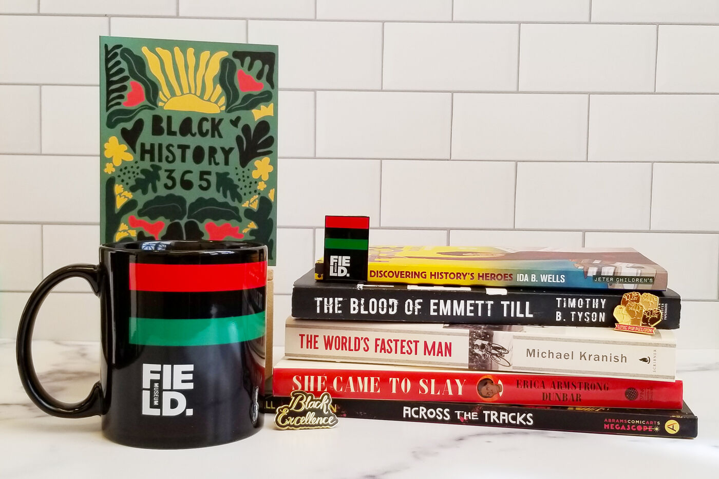 A selection of items available for purchase at the museum store, including a stack of books, a mug, a greeting card and enamel pins.