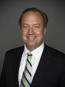 A smiling man in a dark suit, wearing a striped tie.