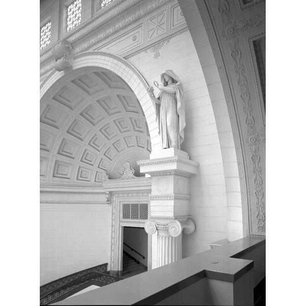 Architectural view the southwest upper corner of Stanley Field Hall, featuring the coffered panel ceiling and a statue of a female figure holding a magnifying glass, representing Research, by artist Henry Hering.
