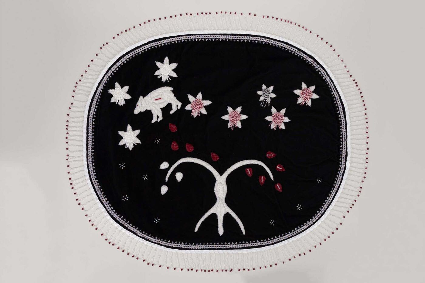 An oval-shaped embroidered artwork with images of a bear and flowers.