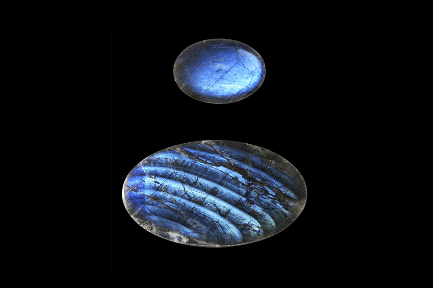 Two examples of rainbow moonstone, a small blue oval disc-shaped stone above a larger oval stone with what appear to be striped markings.