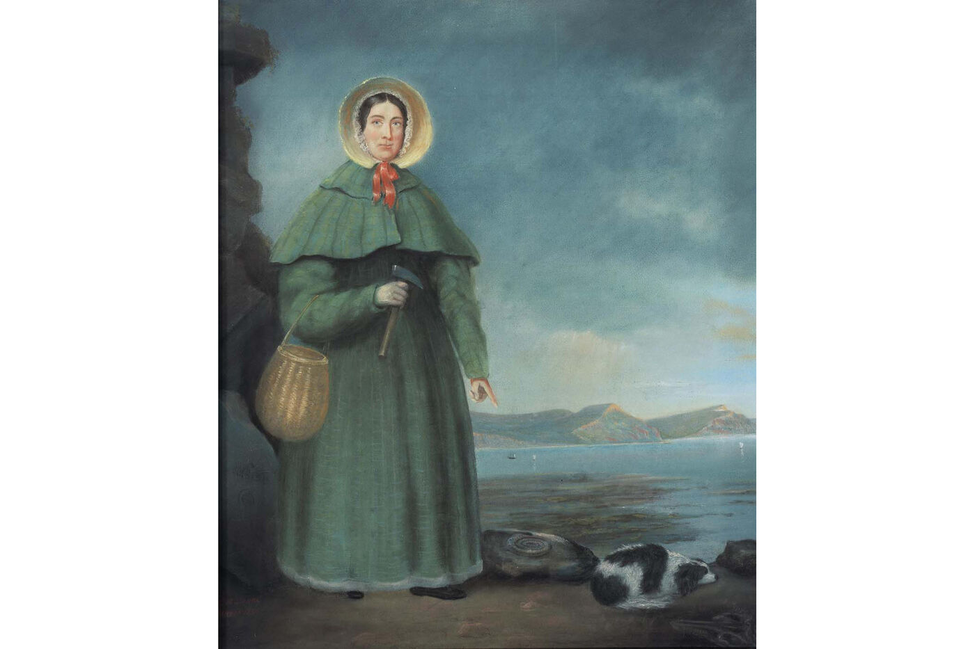 Portrait of a woman in a bonnet and long blue dress holding rock hammer, pointing at fossil next to a spaniel dog lying on the ground.