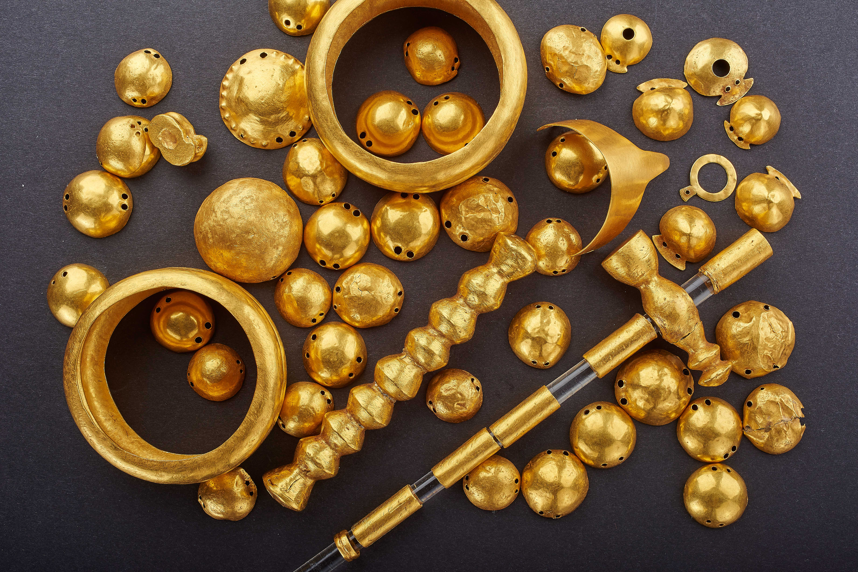 A selection of gold objects, including beads and rings arranged on a black background.