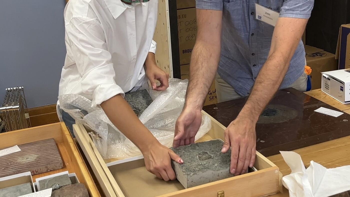 Two people, only visible from the neck down, are removing fossil meteorites from wooden boxes.
