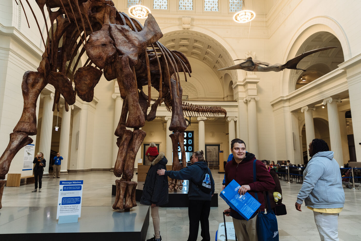 A group of visitors stands in Stanley Field Hall, beneath the Maximo fossil.