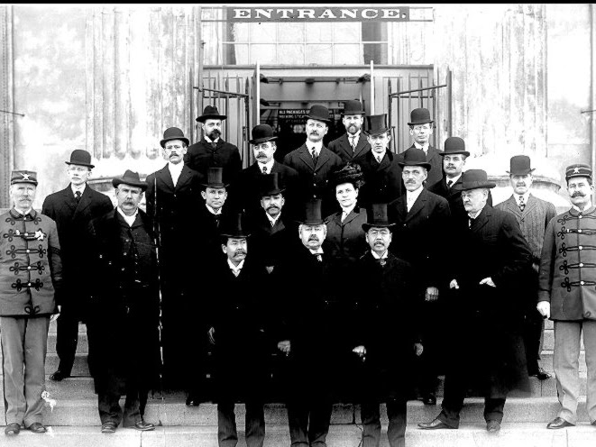 A group of early museum staff stands on steps at the entrance to a building.