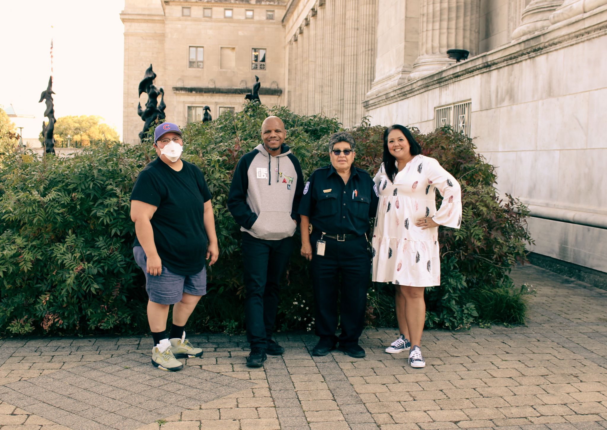 Four people stand in front of a garden outside the Museum.