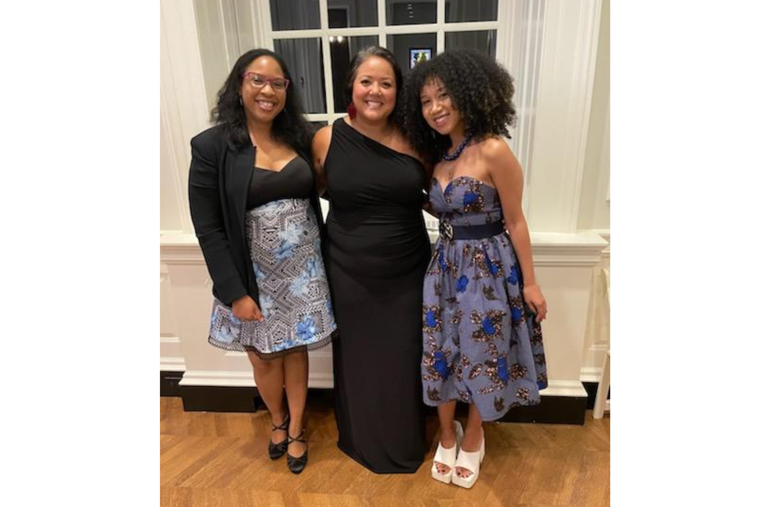 Three women stand together, smiling.