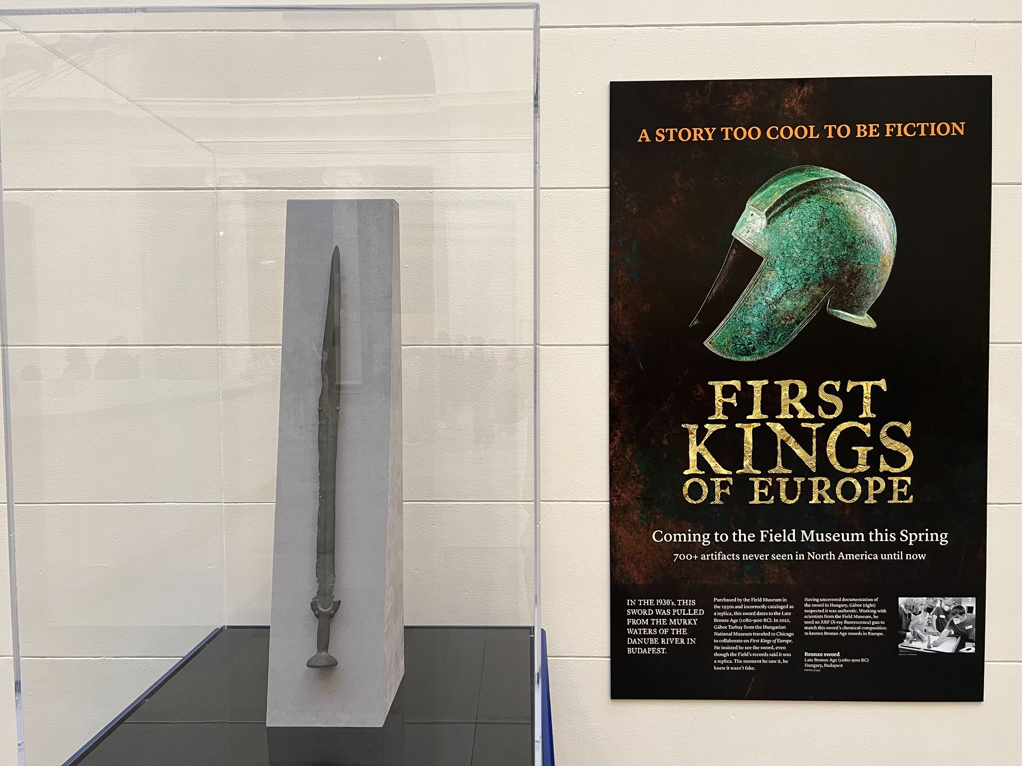 A bronze sword in a display case, next to an exhibition poster for First Kings of Europe.