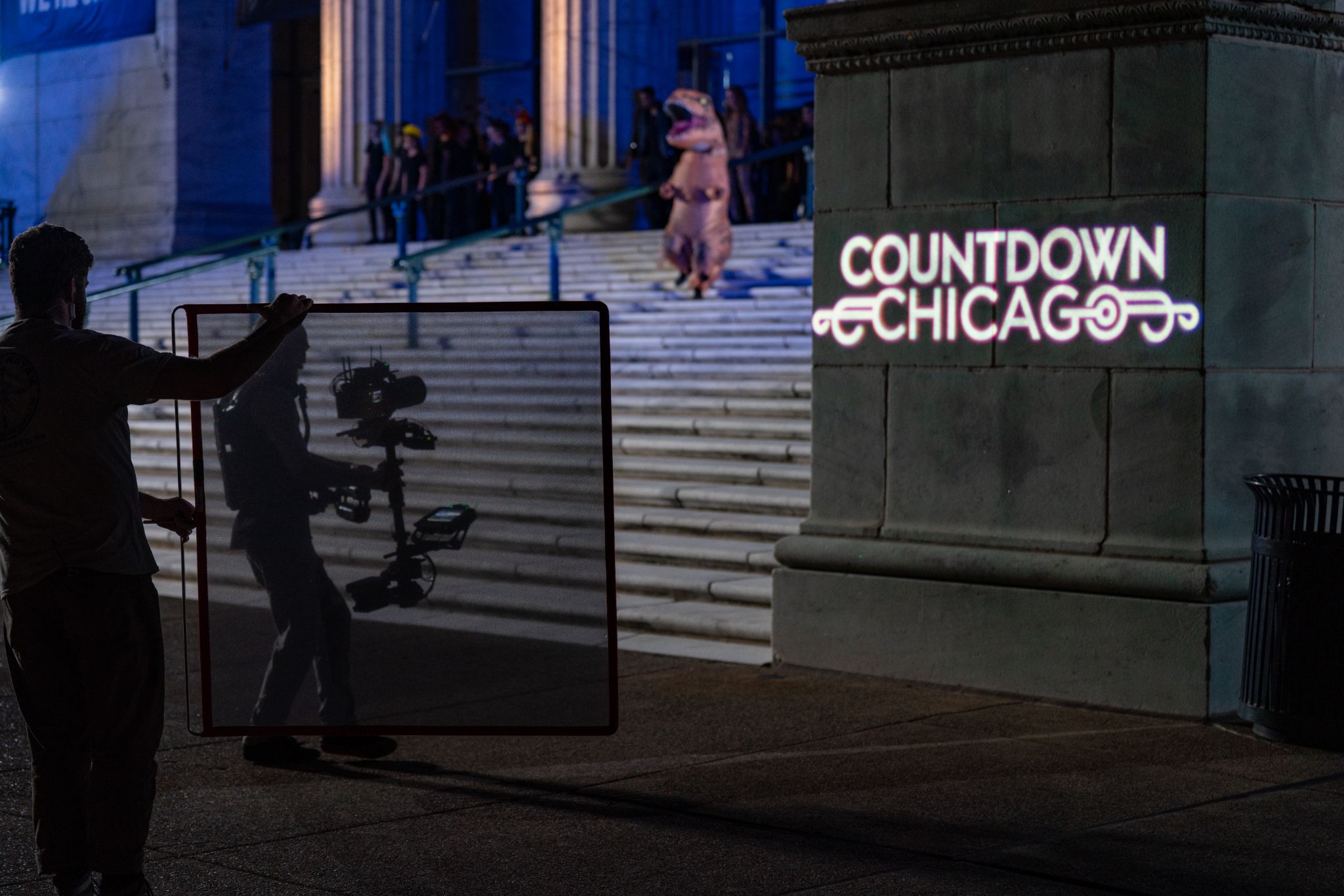 Filming of a television segment on the exterior steps of the Museum, with Inflatable SUE and dancers in the background.