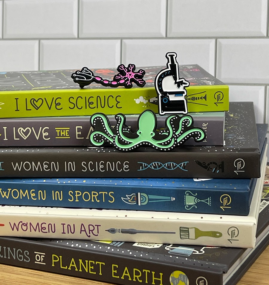 A stack of books and a selection of enamel pins that are available for purchase in the museum store.