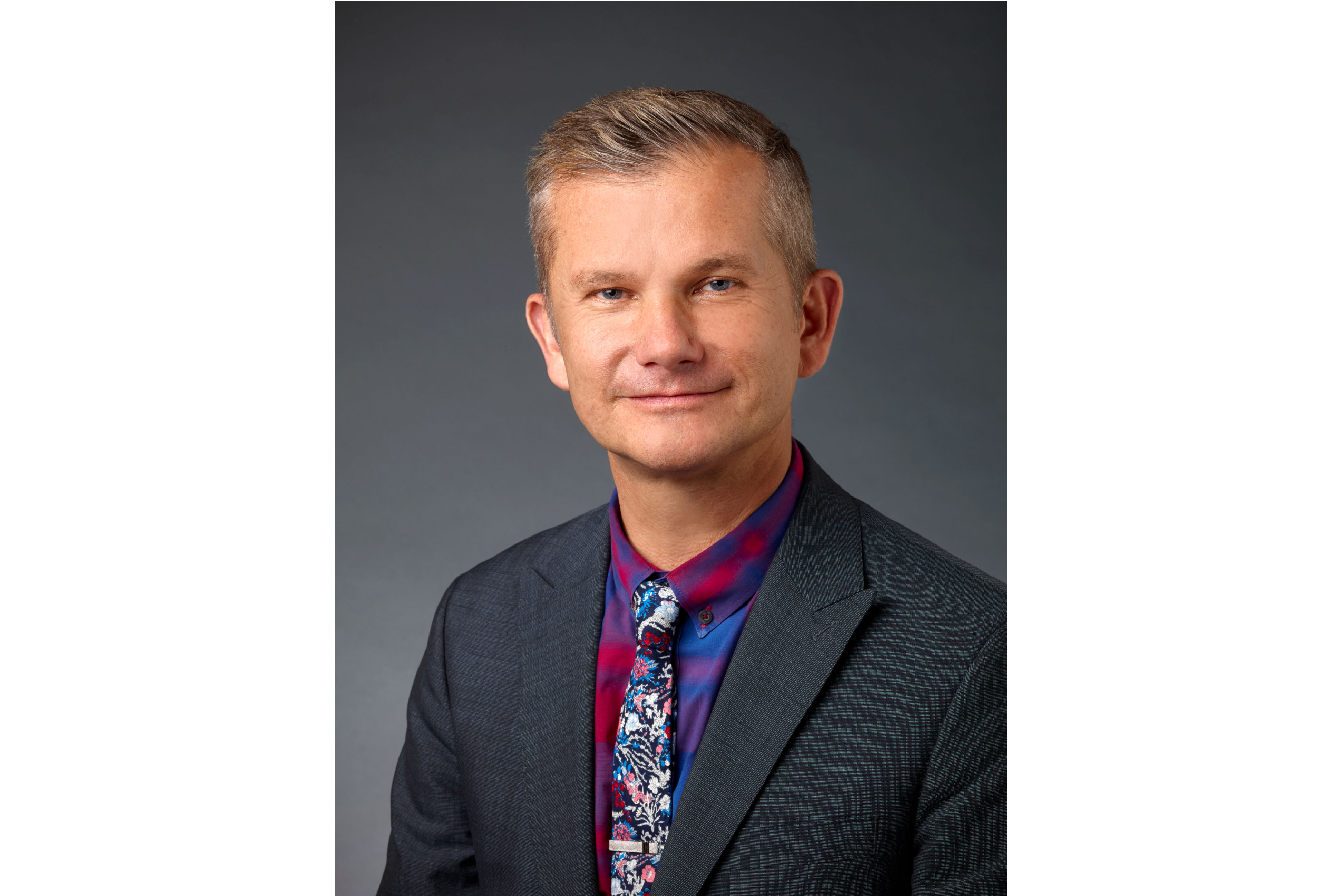 A man wearing a grey suit jacket with a colorful shirt and tie.