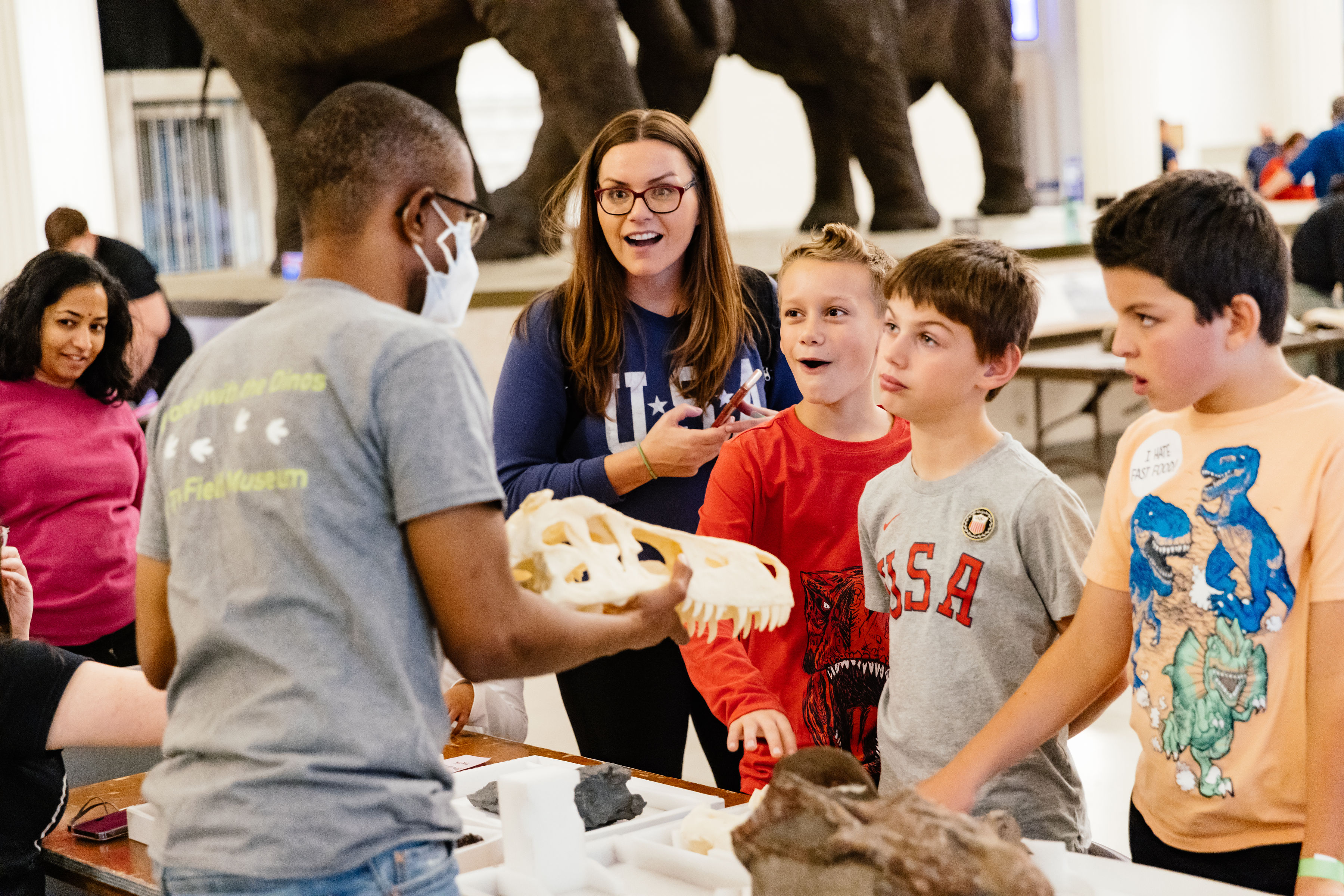 A museum staff memebr holds a skull towards a woman and several boys.