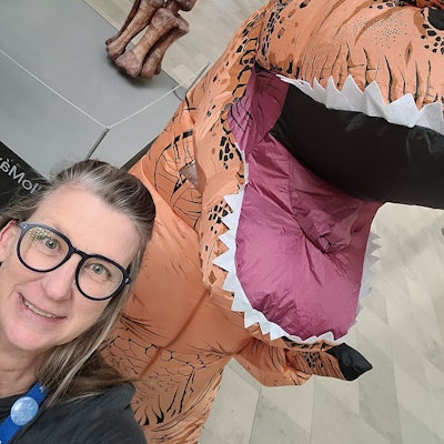 an angled image of a smiling woman next to an inflatable T. rex