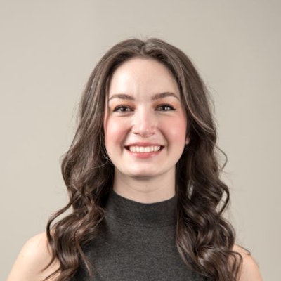 A smiling woman with long brown hair, wearing a gray sleeveless top