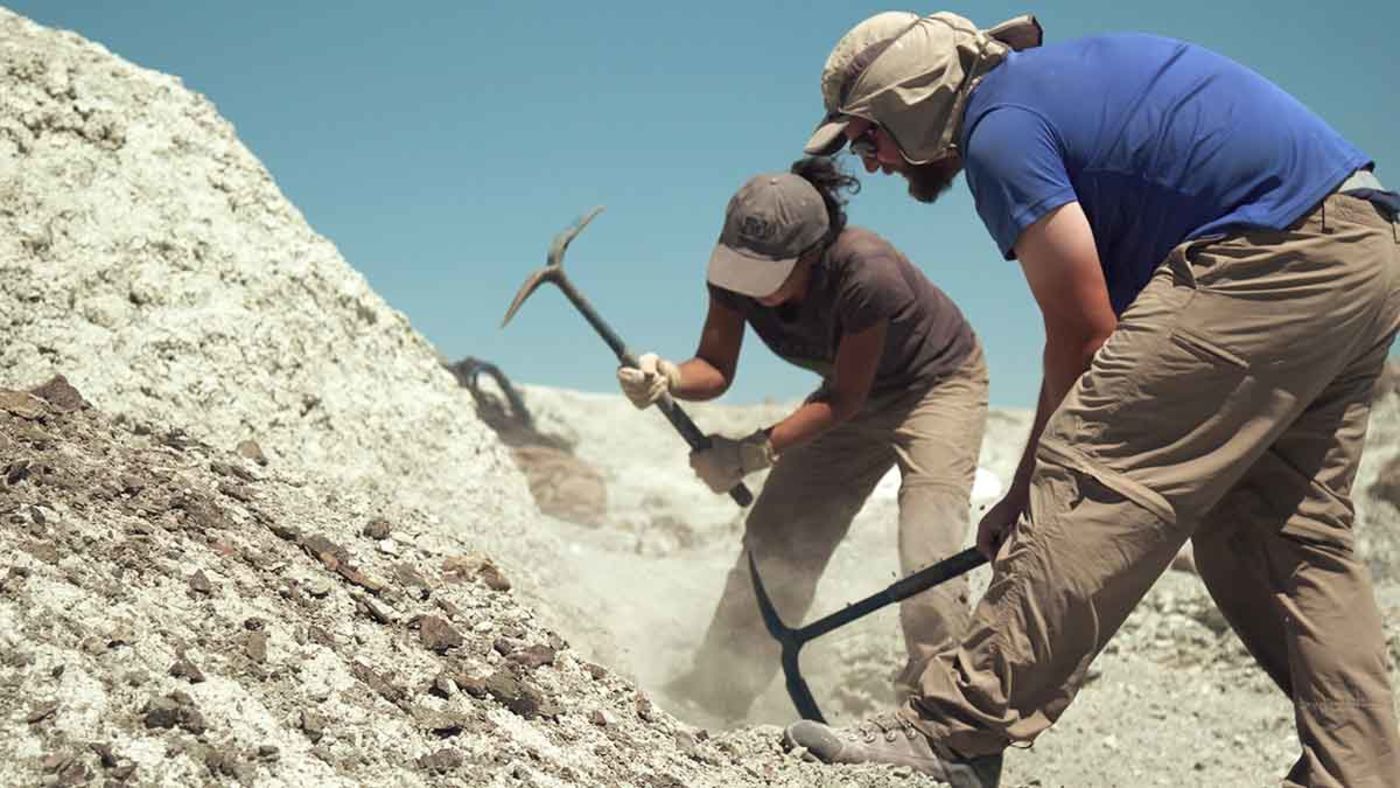 A man and woman with pickaxes digging in a rocky, dusty hill