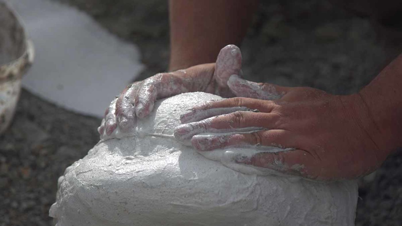Close-up of a person's hands applying wet plaster to a mound