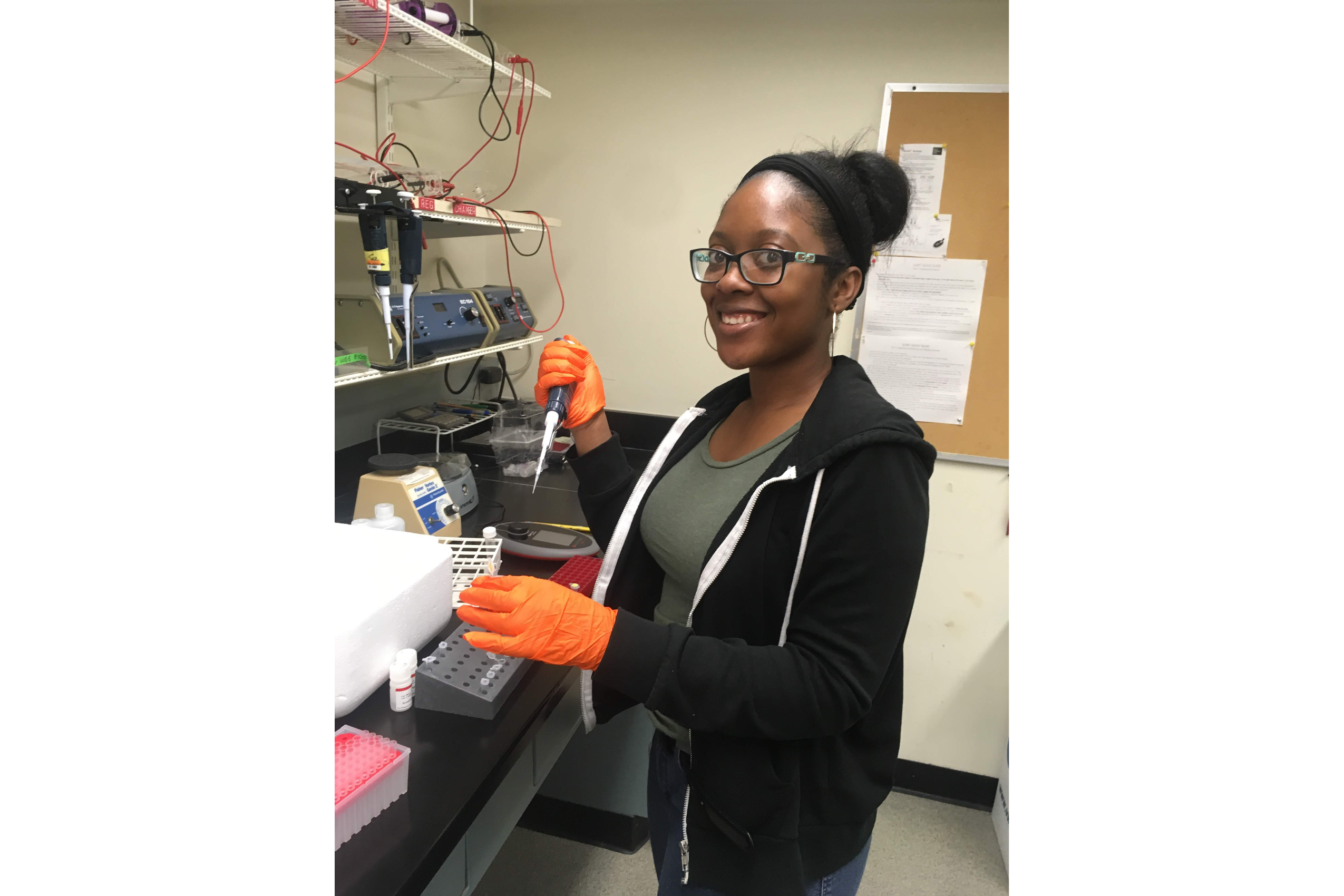 a young woman wearing orange rubber gloves stands in a lab holding instruments