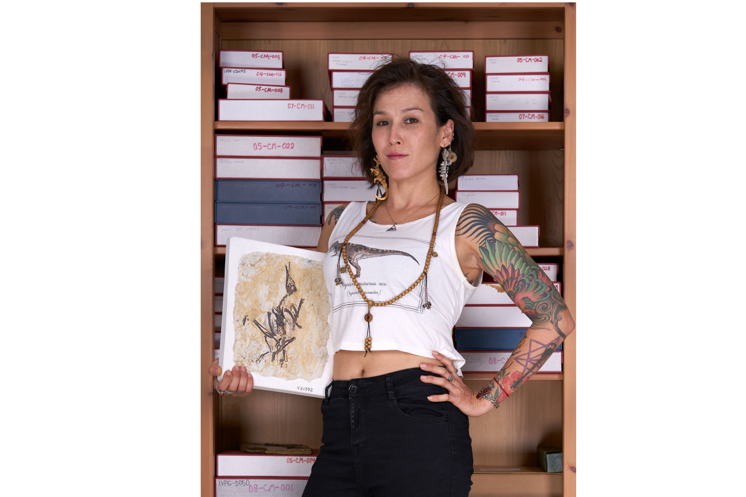 A woman with tattoos on her left arm holds a fossil bird in her right hand