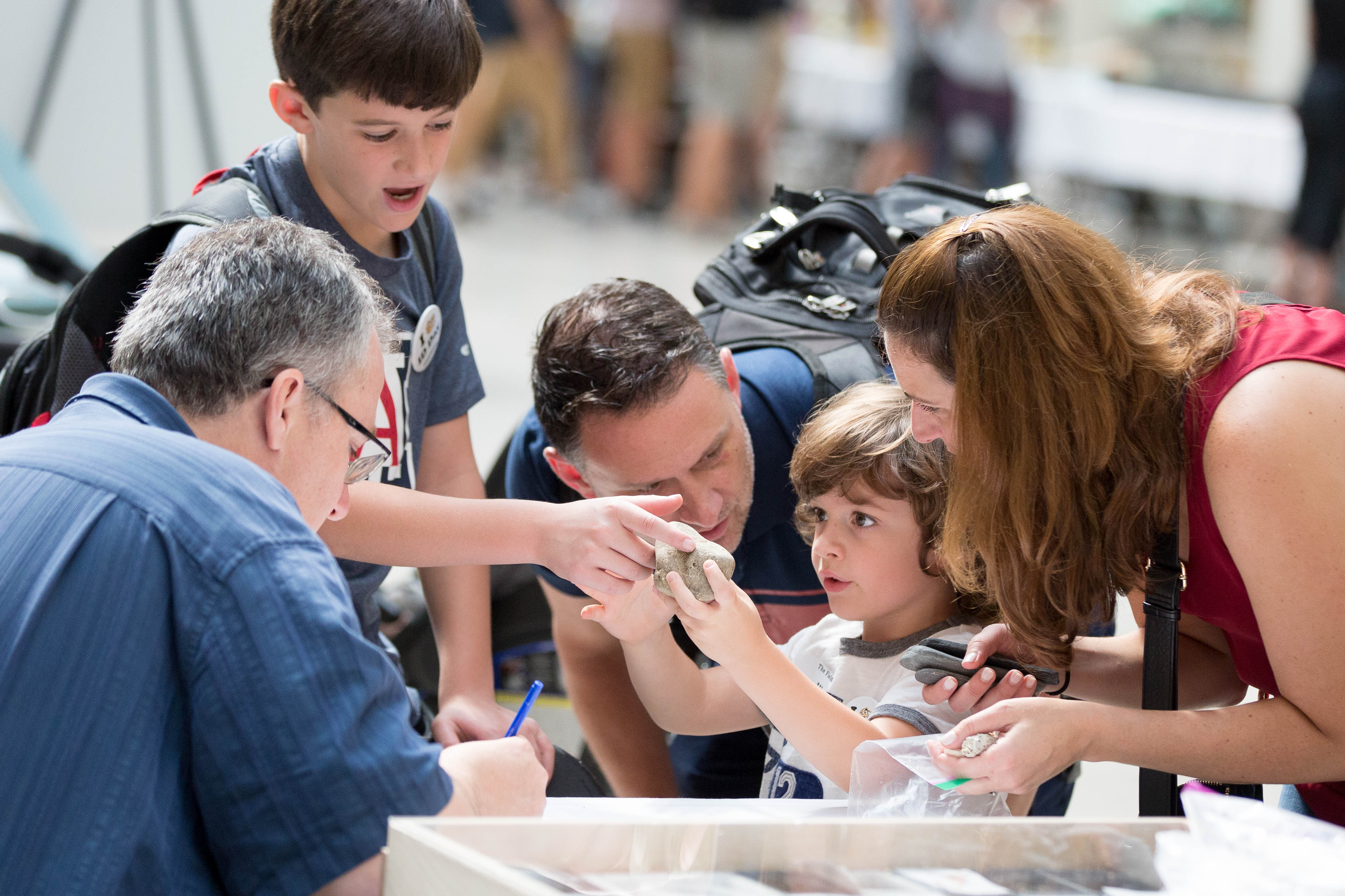 a family bends over looking at a museum specimen as a staff member looks on.