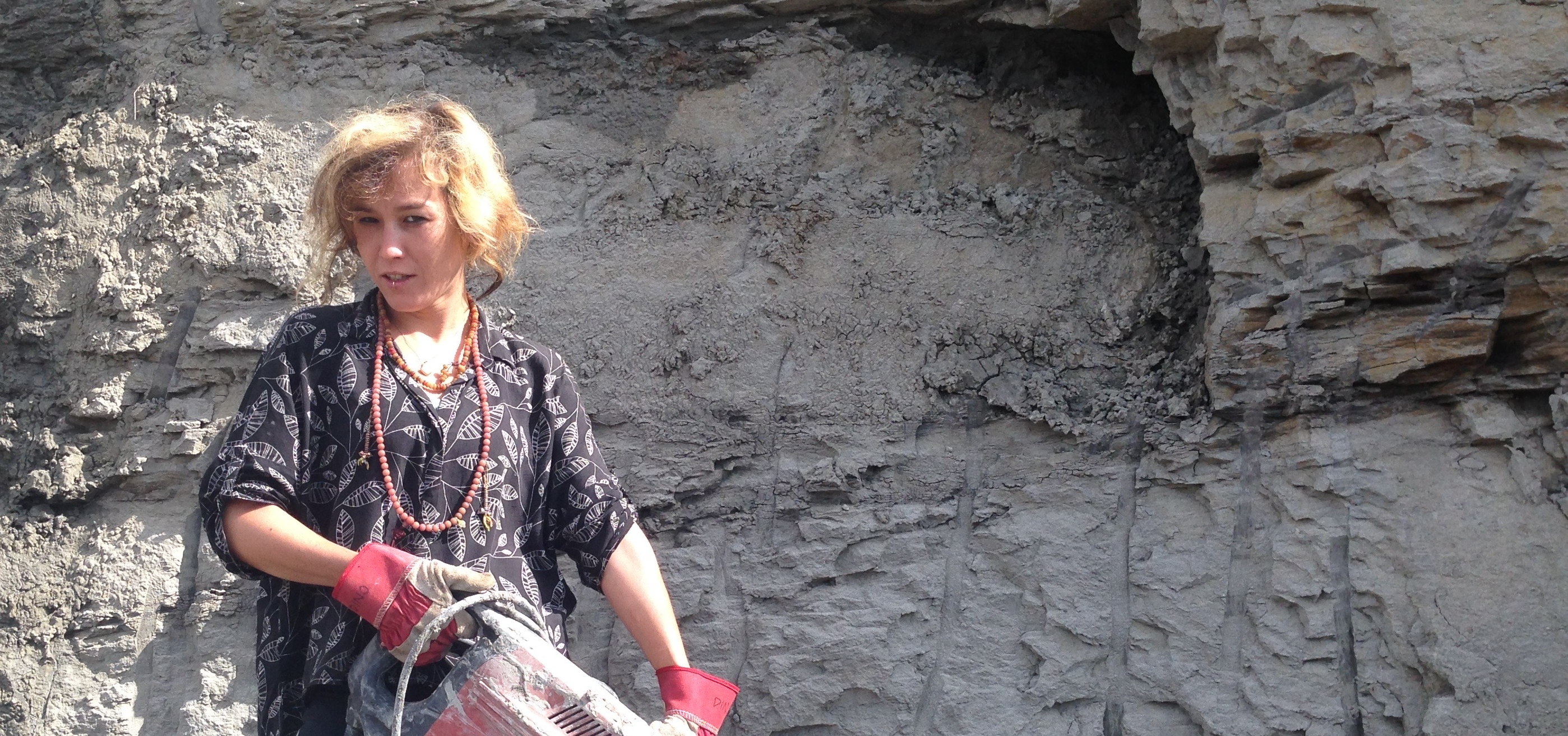 A woman standing in front of a rock face holding a large power drill