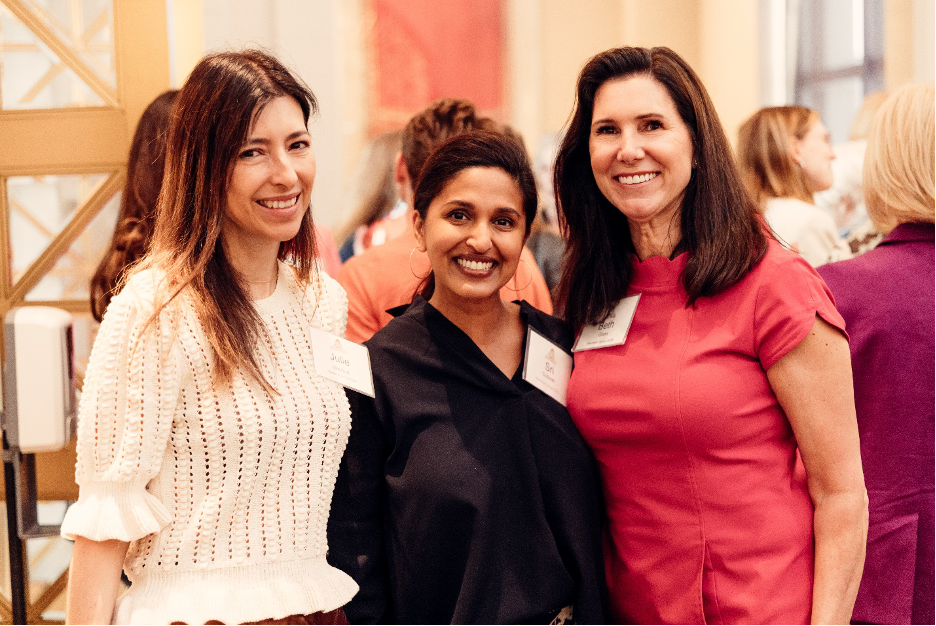 Three women stand side-by-side, smiling at a social event.