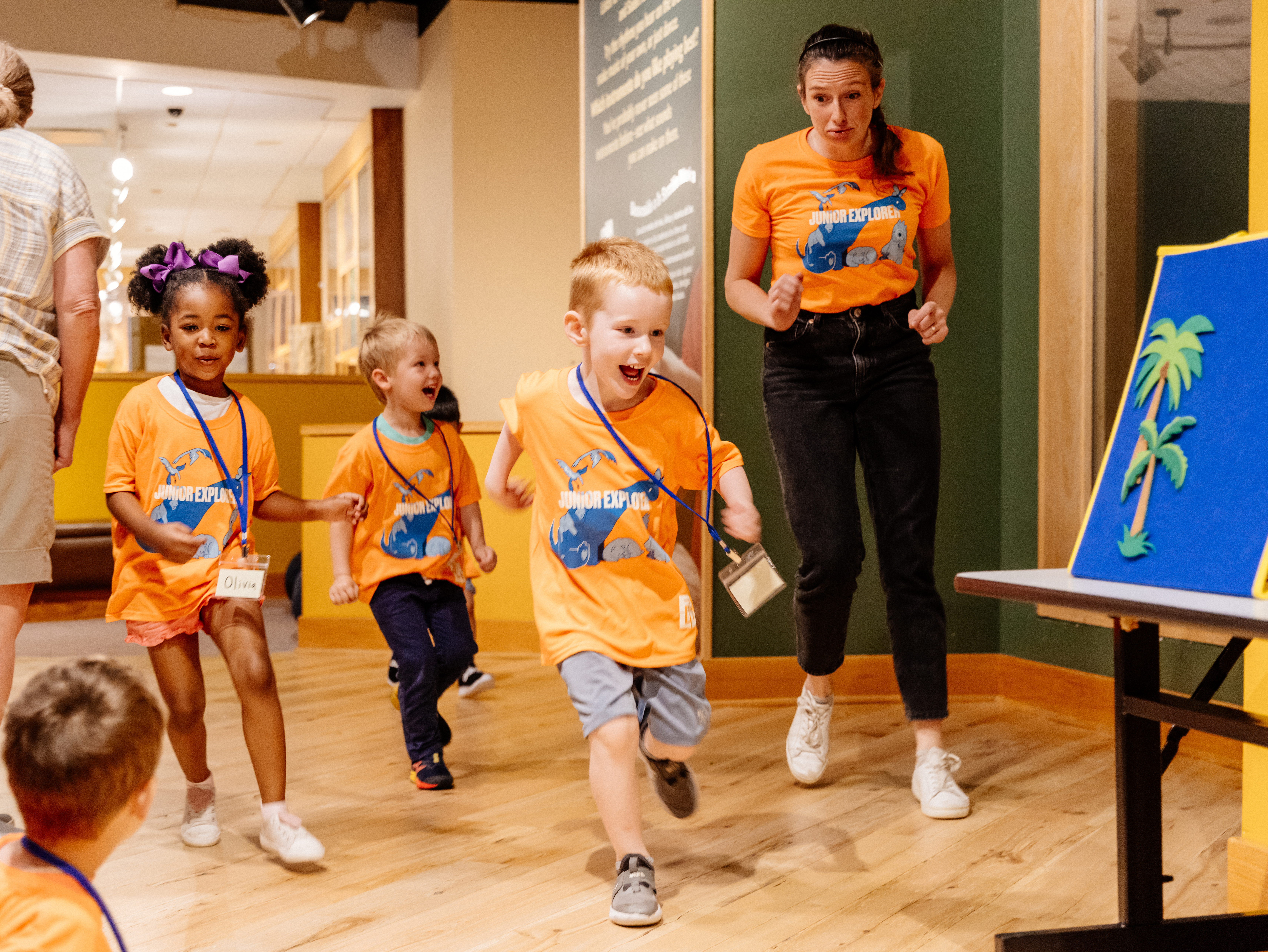 children and a adult walking playfully in the PlayLab; all are wearing matching orange shirts