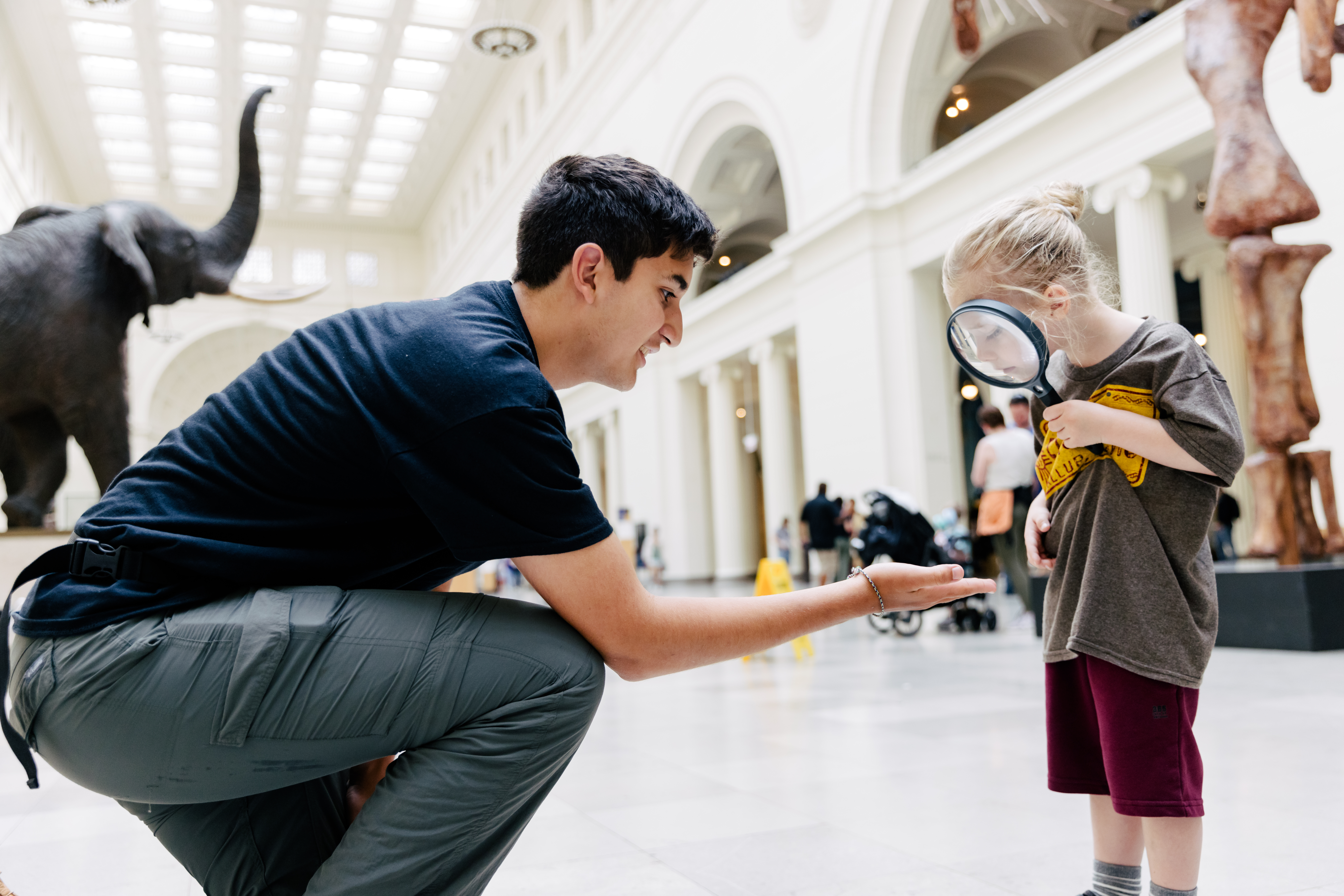 A staff member holding an object for a young visitor to look at with a magnifying glass