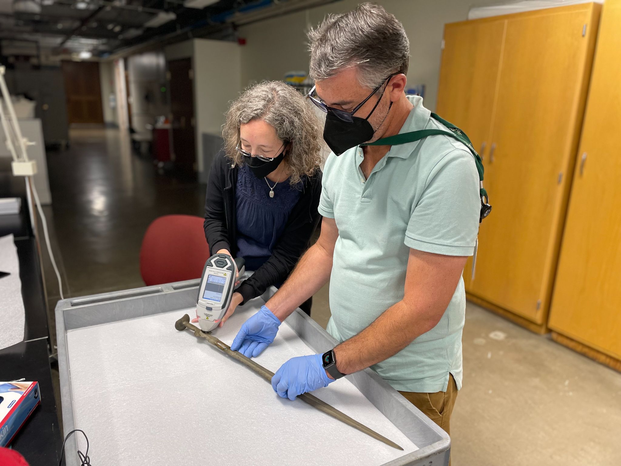 Two people wearing face masks examine an object