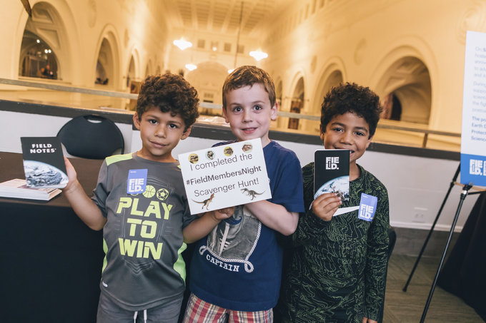 three boys standing next to each other holding up notebooks and a sign saying "I completed the #FieldMembersNight Scavenger Hunt!