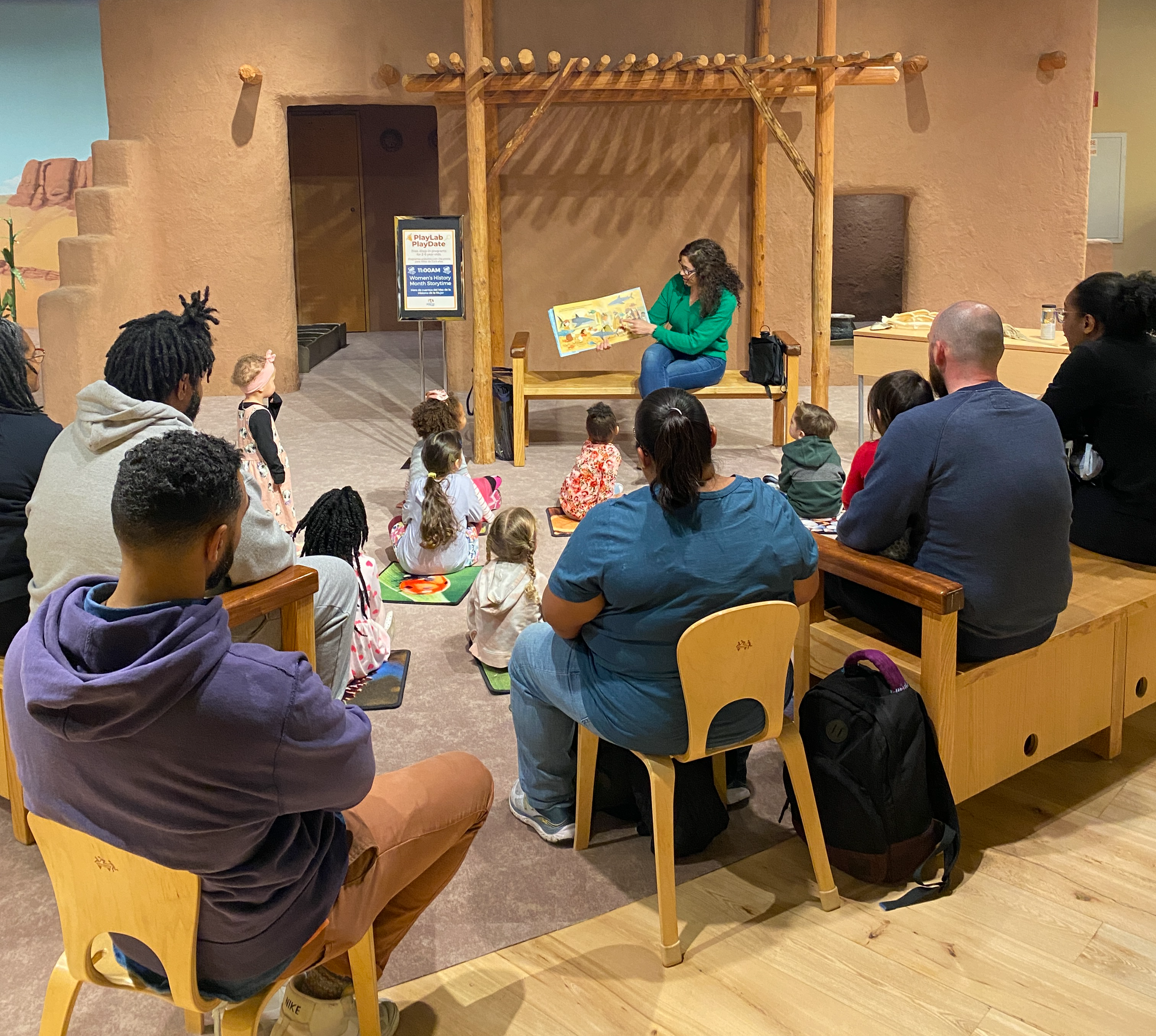A Museum staff member reading a story to visitors in the PlayLab.