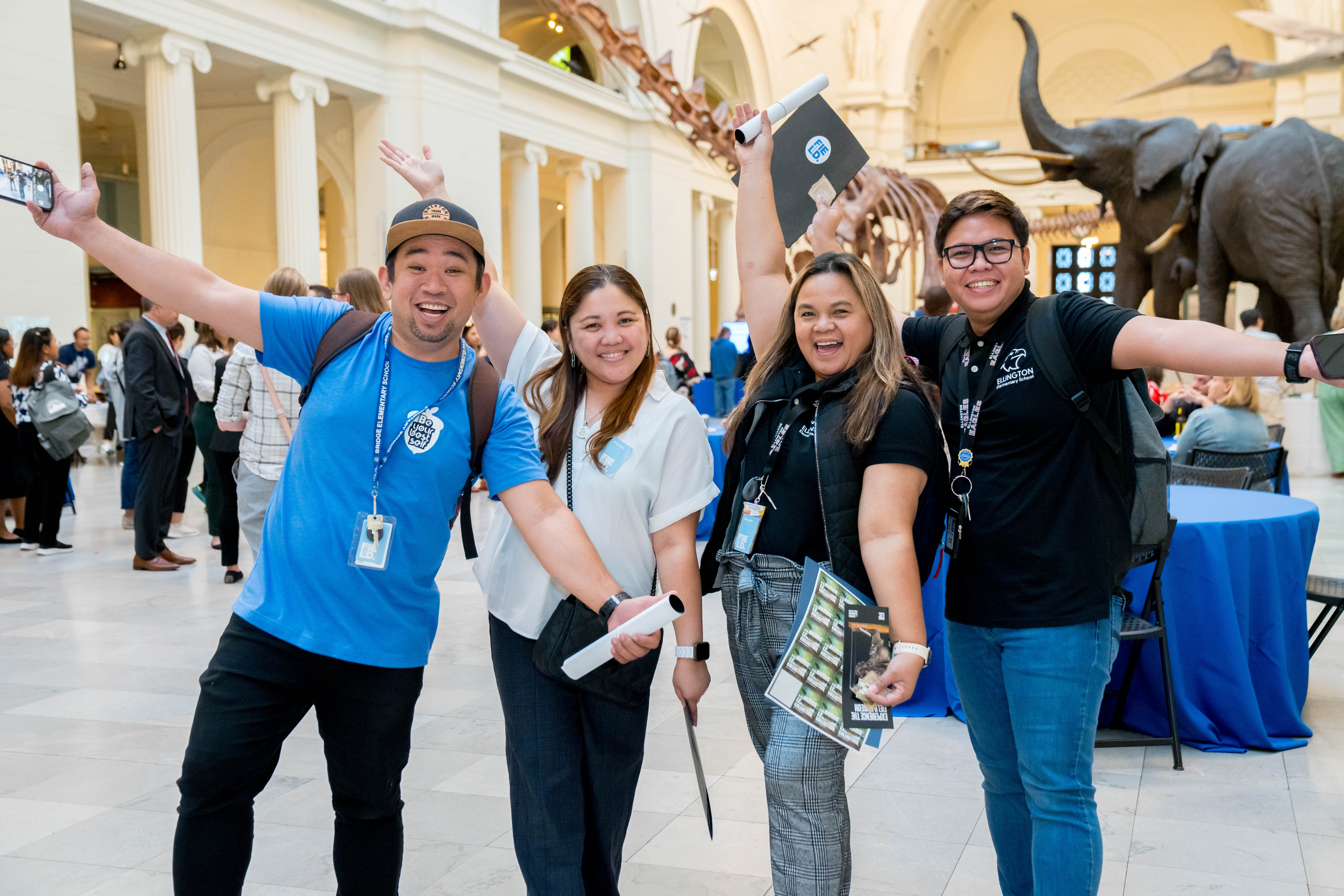 A group of visitors stand together in the museum's main hall, smiling with their arms raised.