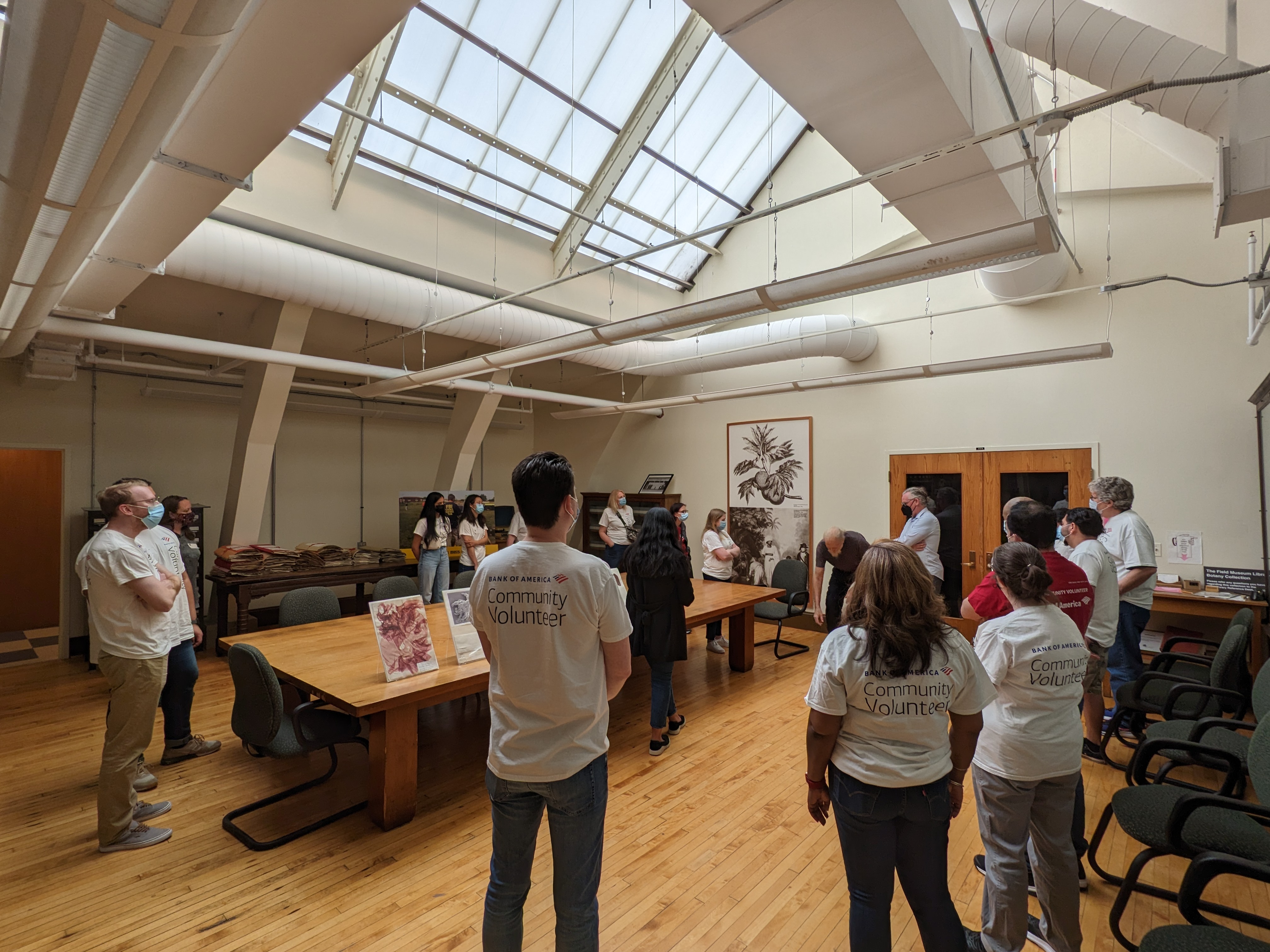 A group of people stand around a large table in a room with a vaulted, glass ceiling.