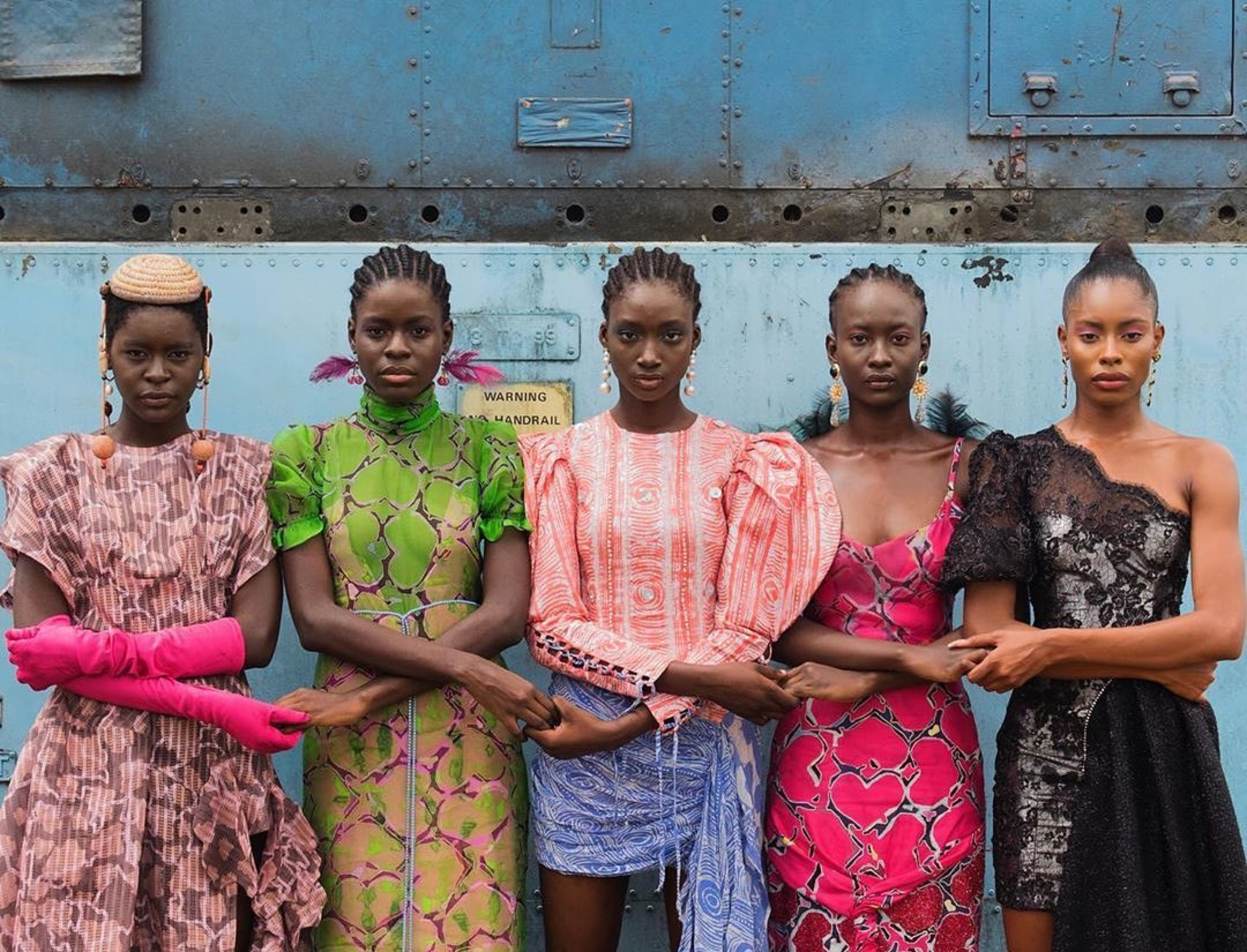 Five young women standing shoulder to shoulder, with their arms crossed in front of them, holding hands with each other