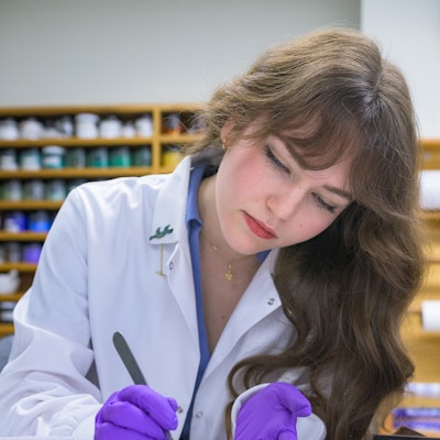 A woman wearing a lab coat and exam gloves. She looks down at a specimen as she examines it with a tool.