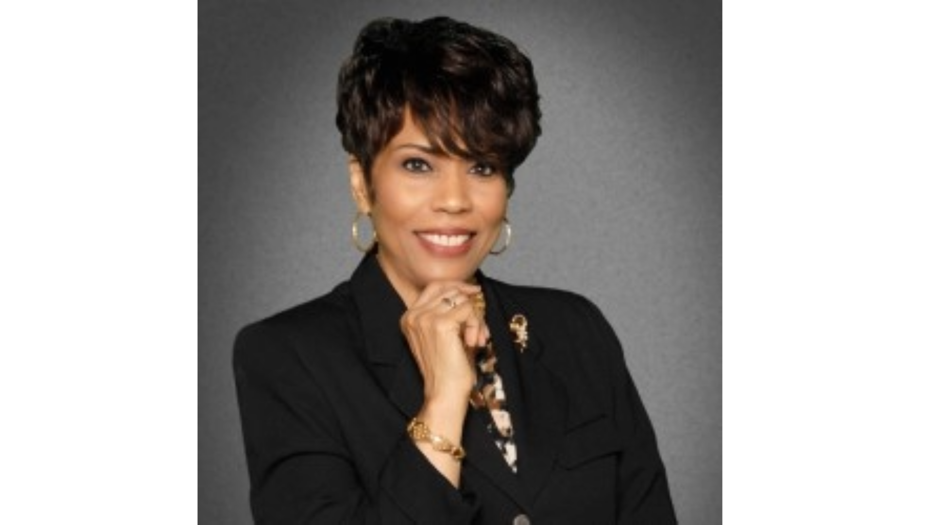 A woman wearing a black suit, holding her hand to her chin