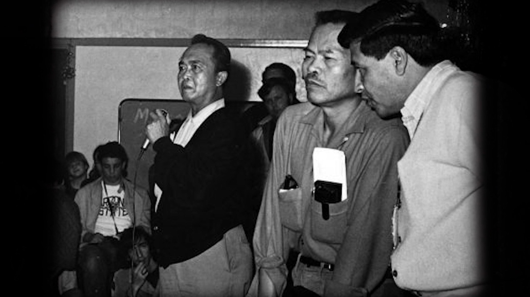 Three men standing together, looking at something out of the picture