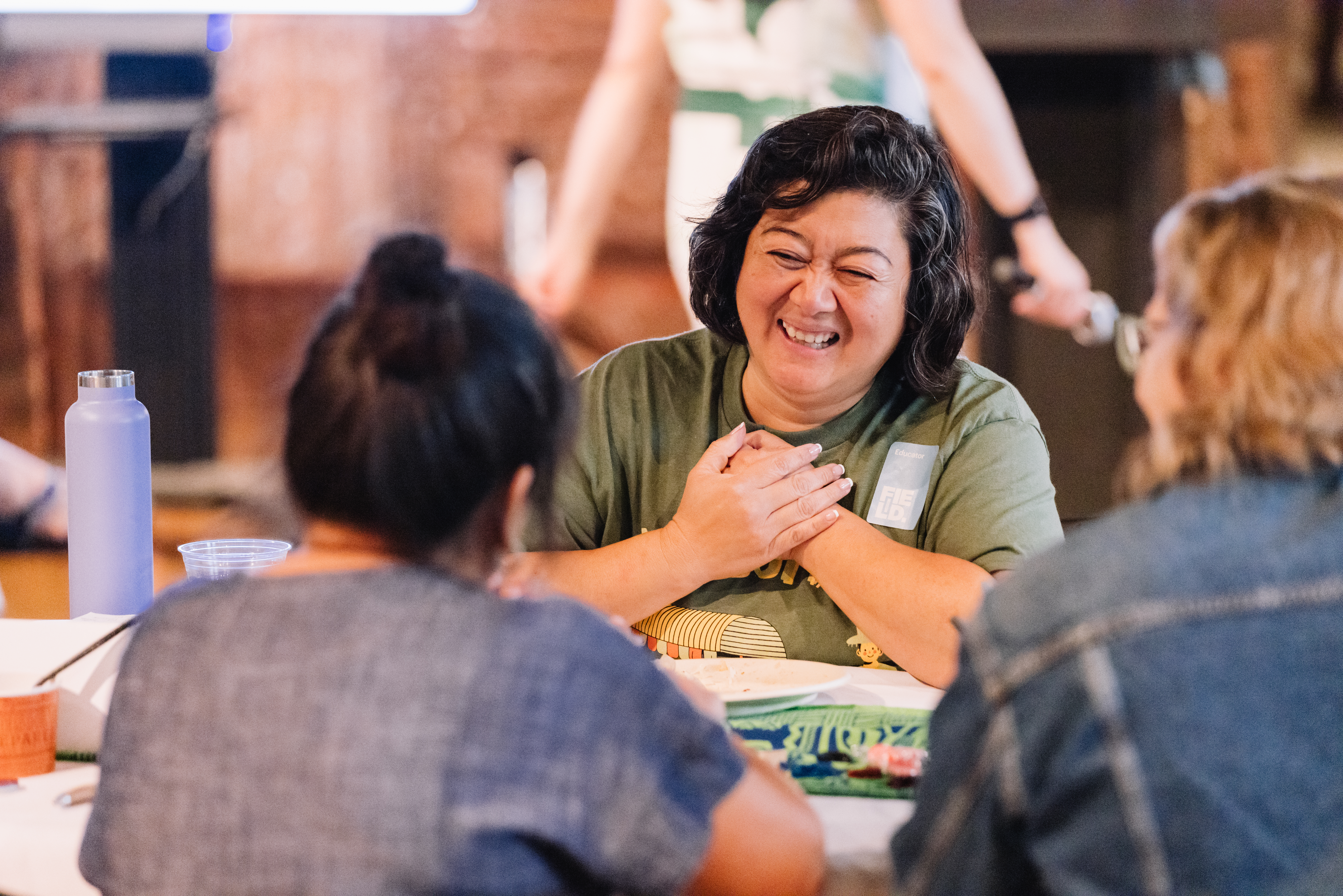 A woman holds her hands to her chest as she smiles at two other women she is seated across from.