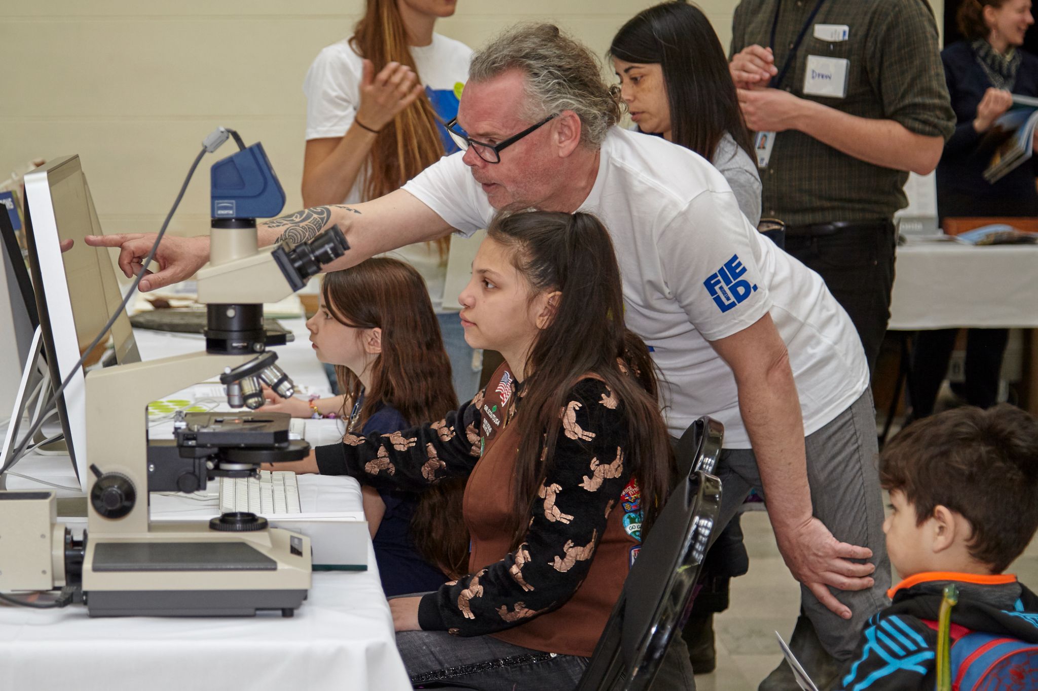 A young person sits at a computer as a man reaches over, pointing at the monitor.