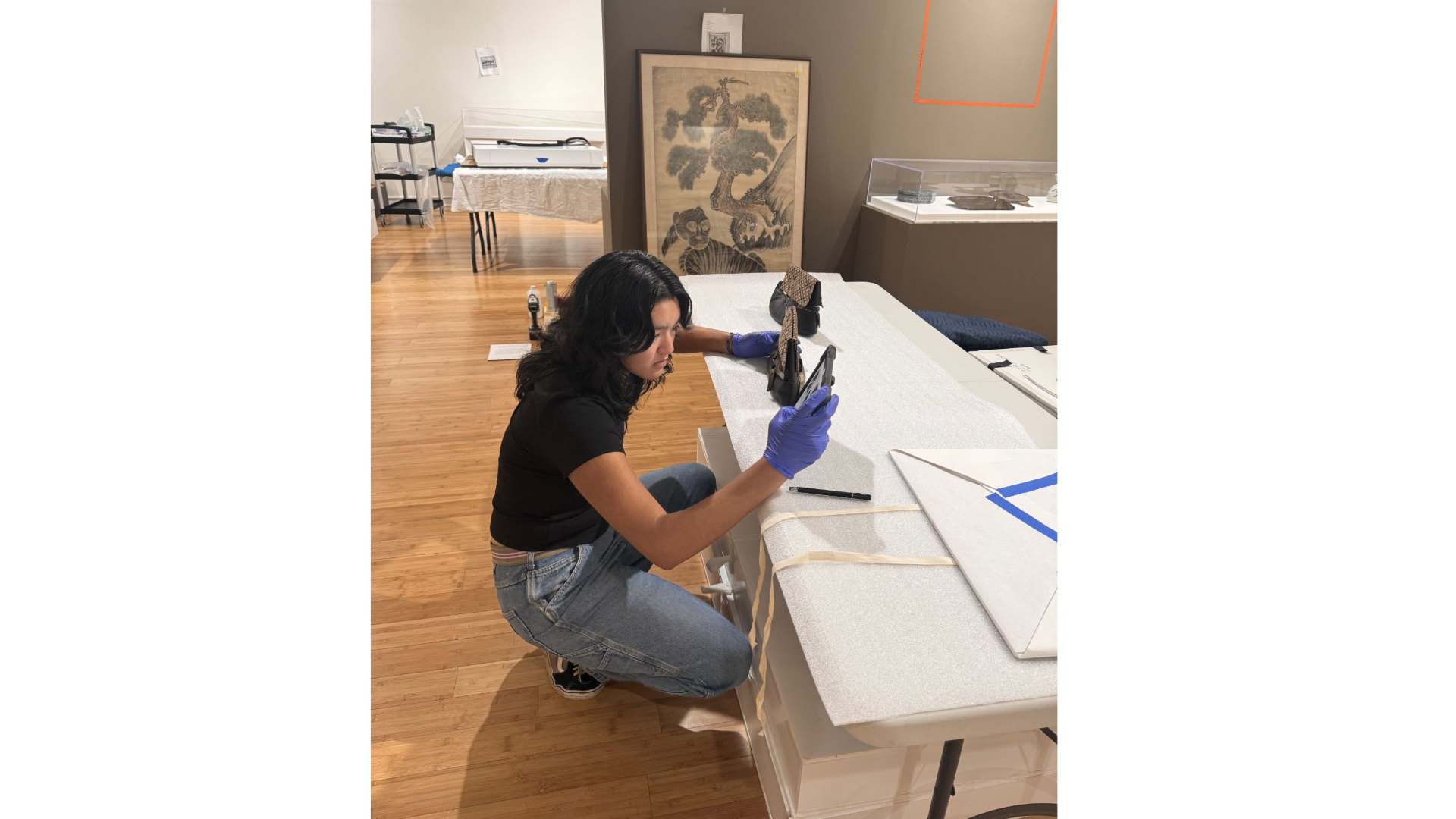 A staff member stoops down at a table, installing an ethnographic item at an onsite visit.