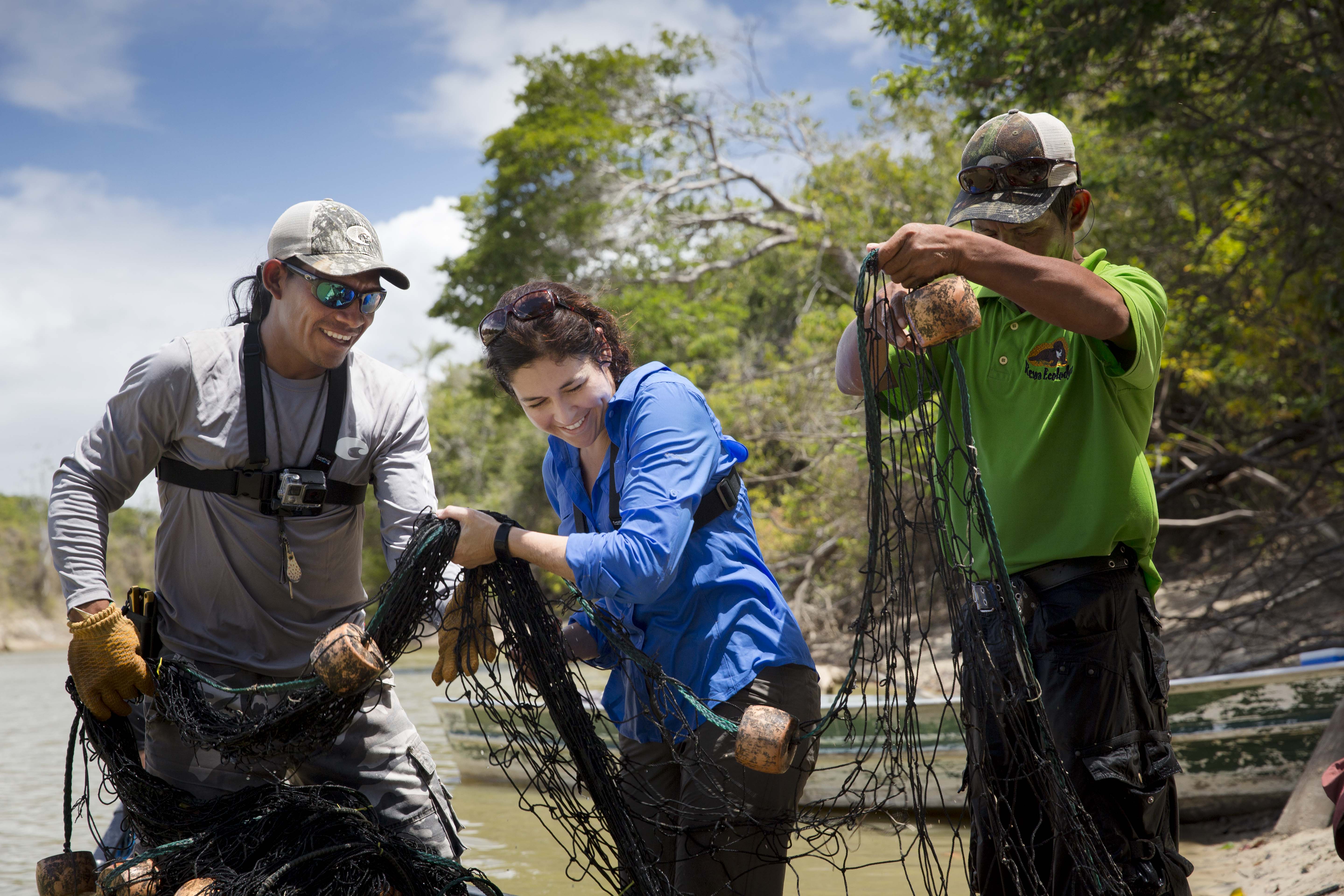 Three people stand in water holding up a large fishing net