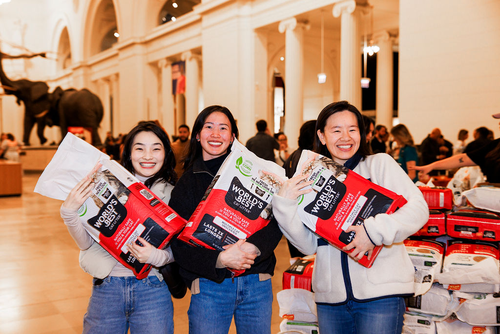 Three women standing in Stanley Field Hall holding red and white bags of World’s Best Cat Litter.