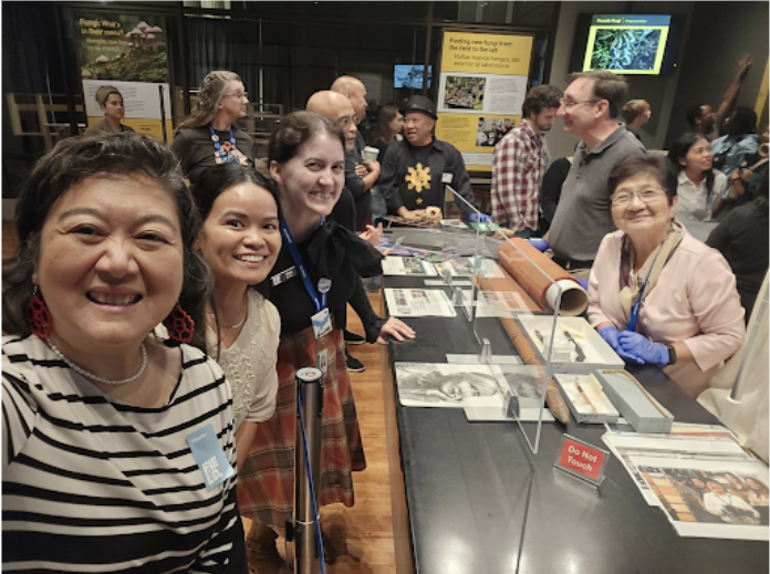 A group of people stand around a table with images and specimens on display.